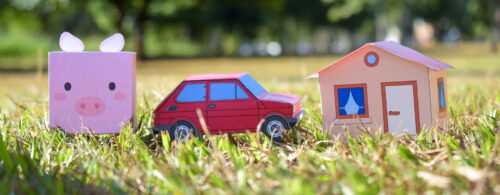 Miniaturas de carro, casa e cofrinho feitas em papel, sobre campo gramado