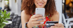 Mulher negra sorrindo com um celular em uma mão e um cartão magnético na outra