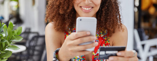 Mulher negra sorrindo com um celular em uma mão e um cartão magnético na outra